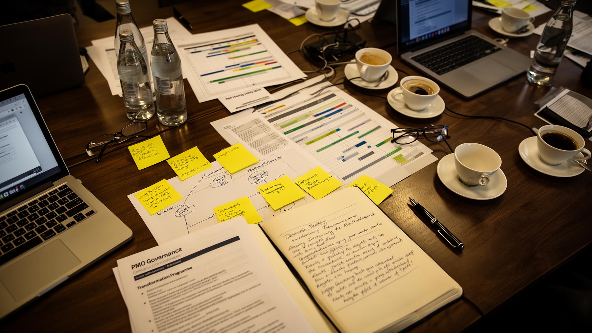 Transformation programme workshop table — roadmap, PMO governance documents and laptops mid-session